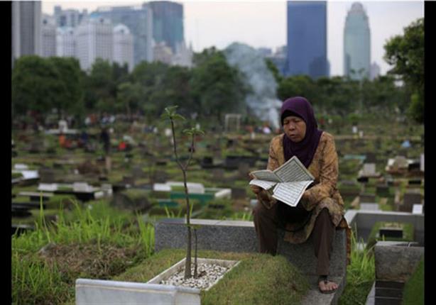 امرأة تقرأ القرآن على قبر زوجها في جاكرتا، إندونيسيا